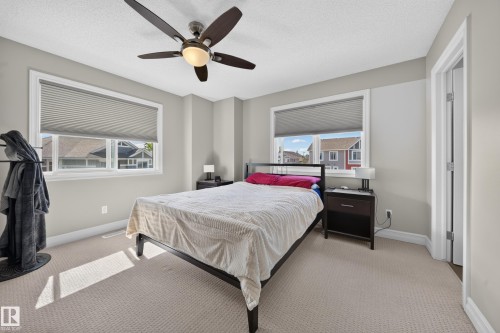 Bedroom featuring a ceiling fan with integrated lighting, two windows with blinds, light-toned carpeting, and neutral wall paint - 64 655 Tamarack Road, Edmonton, AB 