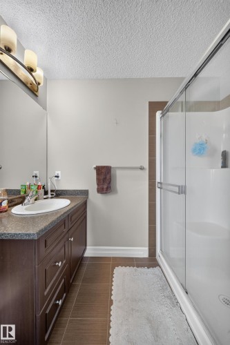 Bathroom featuring a dark wood vanity with a stone-look countertop, an undermount sink, and a mirrored wall - 64 655 Tamarack Road, Edmonton, AB 
