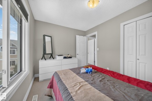 Light-filled room featuring a large window, neutral painted walls, textured carpet flooring, and a ceiling-mounted light fixture - 64 655 Tamarack Road, Edmonton, AB 