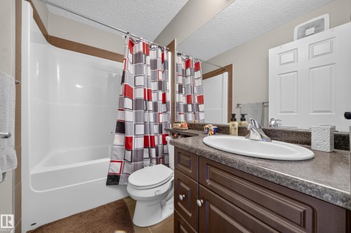 Bathroom featuring a white tub/shower combination, a dark wood-finish vanity with a countertop, an oval undermount sink, and a chrome faucet - 64 655 Tamarack Road, Edmonton, AB 