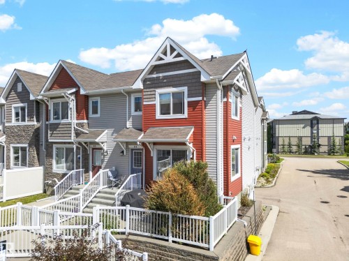 Multi-level townhome featuring a pitched roofline, decorative gable details, and a combination of red and gray siding - 64 655 Tamarack Road, Edmonton, AB 