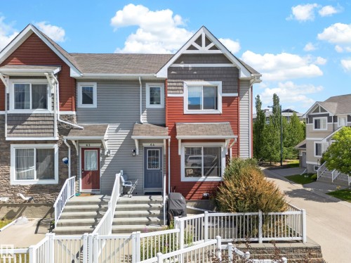 Townhome exterior featuring multi-toned siding, stone veneer accents, and a prominent gable roofline with decorative truss detailing - 64 655 Tamarack Road, Edmonton, AB 