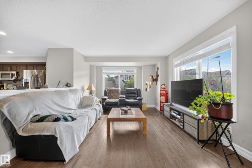 Open-concept living area featuring wood-finish flooring and ample natural light from large windows - 64 655 Tamarack Road, Edmonton, AB 