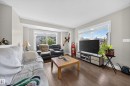 Living area featuring wood-finish flooring, light grey painted walls, and abundant natural light from multiple large windows - 64 655 Tamarack Road, Edmonton, AB 