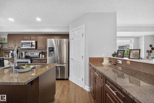 Spacious kitchen featuring an island with an undermount sink, stainless steel appliances, wood-finish flooring, and ample cabinetry - 64 655 Tamarack Road, Edmonton, AB 