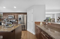 Spacious kitchen featuring an island with an undermount sink, stainless steel appliances, wood-finish flooring, and ample cabinetry - 