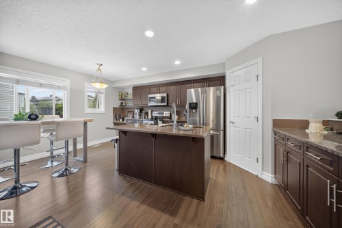 Kitchen featuring dark wood-finish cabinetry, stainless steel appliances, and a central island with a stone countertop - 64 655 Tamarack Road, Edmonton, AB 