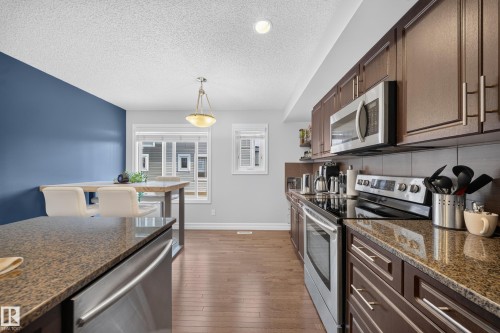 Kitchen featuring dark wood cabinetry, stainless steel appliances, and mottled brown countertops - 64 655 Tamarack Road, Edmonton, AB 