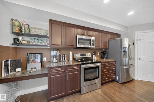Kitchen featuring wood-finish flooring, dark wood cabinetry, and stainless steel appliances - 64 655 Tamarack Road, Edmonton, AB 