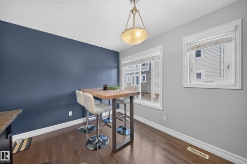 Dining area featuring dark wood-finish flooring, a contemporary overhead light fixture, white trim, and a prominent accent wall - 64 655 Tamarack Road, Edmonton, AB 