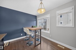 Dining area featuring dark wood-finish flooring, a contemporary overhead light fixture, white trim, and a prominent accent wall - 
