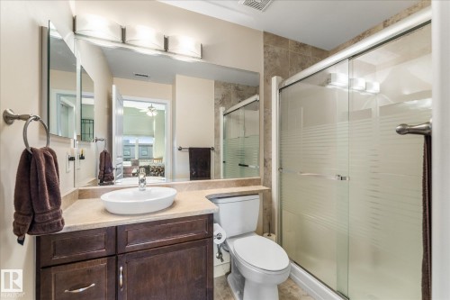 Bathroom featuring a dark wood-finish vanity with an oval vessel sink, a light-toned countertop, a large wall-mounted mirror, and a glass-enclosed shower with frosted accents - 408 11140 68 Avenue, Edmonton, AB 