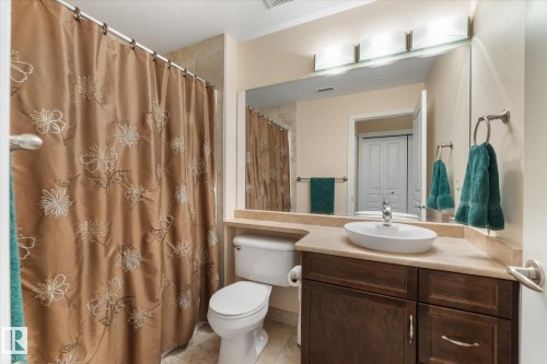 Bathroom featuring a vessel sink set in a stone-finish countertop, dark wood-finish vanity, and an integrated mirror with overhead lighting - 408 11140 68 Avenue, Edmonton, AB 