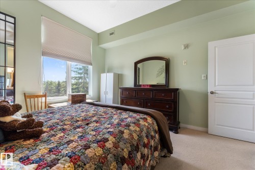 Spacious room featuring a large window with natural scenery, light green walls, and light-colored carpet flooring - 408 11140 68 Avenue, Edmonton, AB 