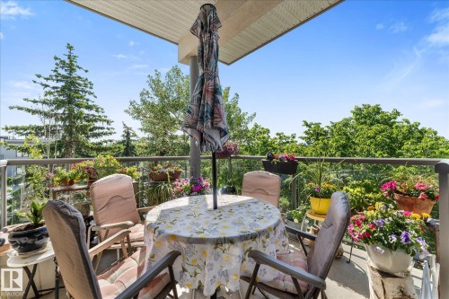 Balcony featuring a glass railing, concrete flooring, and surrounding mature trees - 408 11140 68 Avenue, Edmonton, AB 