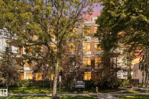 Multi-story building featuring a facade with multiple windows, some with visible balconies, and ground-level landscaping with mature trees and green lawn - 408 11140 68 Avenue, Edmonton, AB 