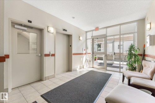 Common area featuring tile flooring, elevator access, and a glass-paneled entry door - 408 11140 68 Avenue, Edmonton, AB 