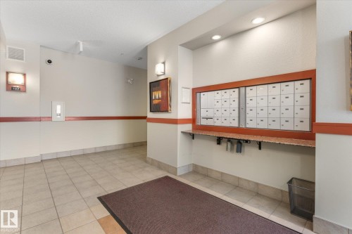 Building entrance featuring large format tile flooring, recessed lighting, wall-mounted sconces, and a communal mailbox system with a granite-style shelf - 408 11140 68 Avenue, Edmonton, AB 