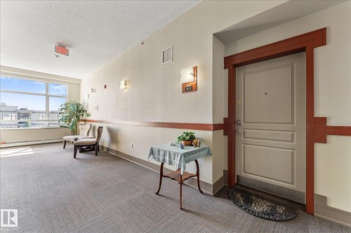 Hallway with patterned carpet flooring, large windows, and wall sconces providing ambient lighting - 408 11140 68 Avenue, Edmonton, AB 