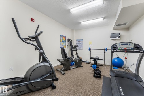 Dedicated fitness area featuring carpeted flooring, white painted walls, and fluorescent lighting - 408 11140 68 Avenue, Edmonton, AB 