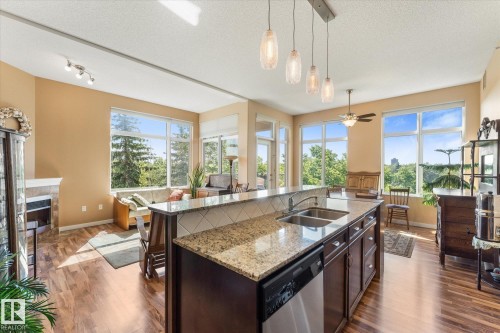 Kitchen island featuring a double-basin sink, integrated dishwasher, and granite countertop - 408 11140 68 Avenue, Edmonton, AB 