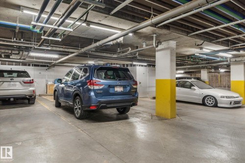 Underground parking garage featuring concrete flooring, exposed overhead piping, fluorescent lighting, and painted structural columns - 408 11140 68 Avenue, Edmonton, AB 