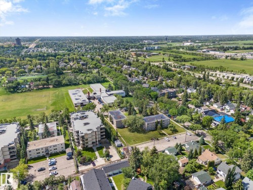 Aerial perspective showcasing a residential area with varied housing structures, extensive green spaces, and mature tree canopies - 408 11140 68 Avenue, Edmonton, AB 