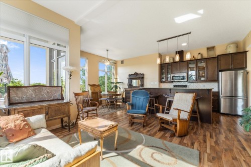 Open-concept living space featuring wood-finish flooring, a full kitchen with stainless steel appliances, and abundant natural light from large windows - 408 11140 68 Avenue, Edmonton, AB 