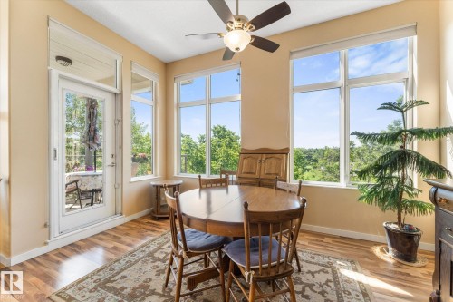 Room featuring large multi-pane windows, a glass-panel door, wood-finish flooring, and a ceiling fan with integrated lighting - 408 11140 68 Avenue, Edmonton, AB 