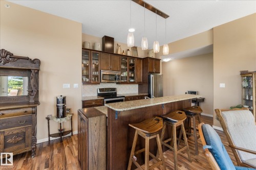 Kitchen featuring wood-finish flooring, dark wood cabinetry, a tiled backsplash, and stainless steel appliances - 408 11140 68 Avenue, Edmonton, AB 