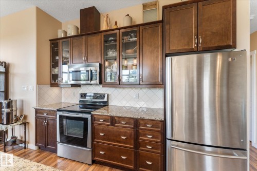 Kitchen featuring wood-finish cabinetry, stainless steel appliances, granite countertops, tile backsplash, and wood-finish flooring - 408 11140 68 Avenue, Edmonton, AB 