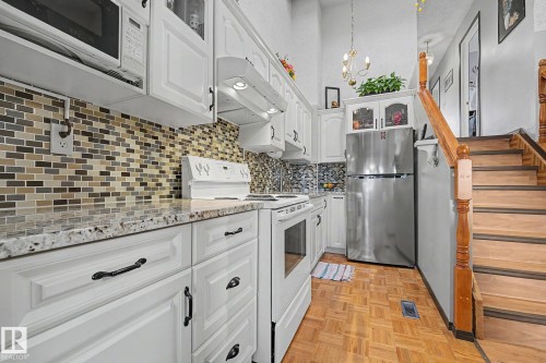 Kitchen featuring white cabinetry with dark hardware, a mosaic tile backsplash, and light-colored countertops - 10242 161 Street, Edmonton, AB 
