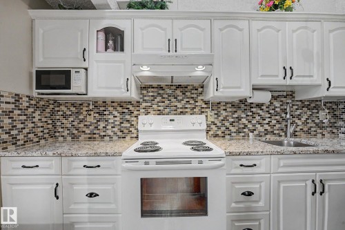 Kitchen featuring white cabinetry with dark hardware, a mosaic tile backsplash, speckled countertops, an electric range, and an undermount sink with a gooseneck faucet - 10242 161 Street, Edmonton, AB 