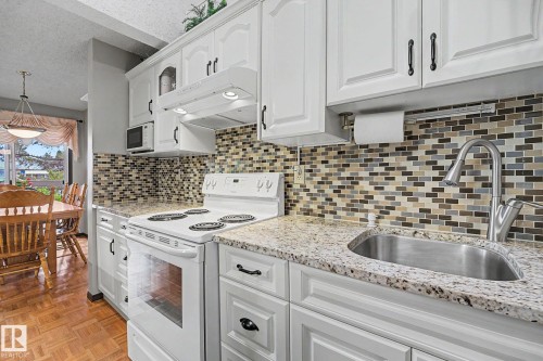 Kitchen featuring white cabinetry with dark hardware, a mosaic tile backsplash, and light-toned countertops - 10242 161 Street, Edmonton, AB 