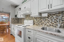 Kitchen featuring white cabinetry with dark hardware, a mosaic tile backsplash, and light-toned countertops - 