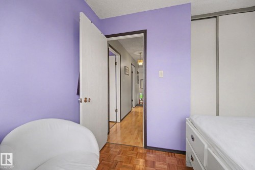 Room featuring a white sliding door closet, light purple wall, and wood-finish parquet flooring - 10242 161 Street, Edmonton, AB 