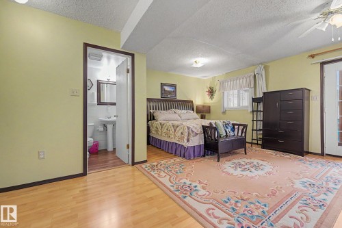 Spacious bedroom featuring wood-finish flooring, a ceiling fan with integrated lighting, and a white paneled door - 10242 161 Street, Edmonton, AB 