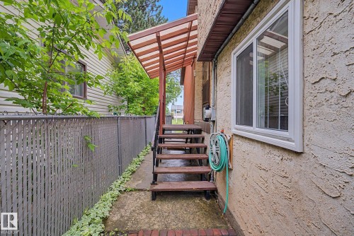 Exterior stucco finish with a modern white-framed window, covered porch stairs, and a chain-link fence featuring privacy slats - 10242 161 Street, Edmonton, AB 