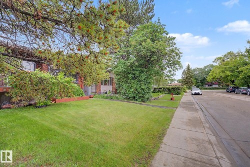 Front exterior featuring a brick facade, mature trees, a manicured lawn, and a concrete sidewalk - 10242 161 Street, Edmonton, AB 