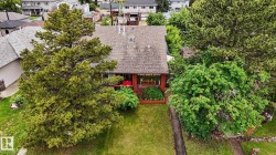 Gable roof home featuring mature trees, a front lawn, and a paved walkway - 