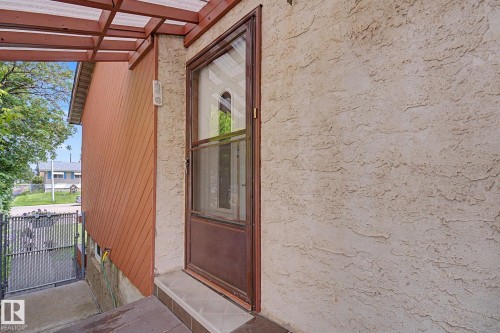 Entryway featuring a brown full-light storm door, textured stucco siding, and a slatted wood awning with a translucent roof - 10242 161 Street, Edmonton, AB 