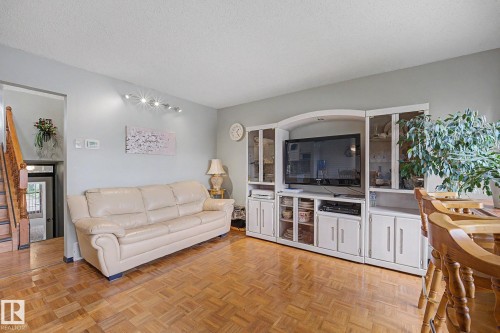 Parquet wood-finish flooring throughout, featuring a built-in entertainment unit with glass-front display cabinets and integrated storage - 10242 161 Street, Edmonton, AB 