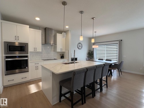 Modern kitchen featuring a large island with a waterfall countertop, integrated sink, and pendant lighting - 9952 227 Street, Edmonton, AB 