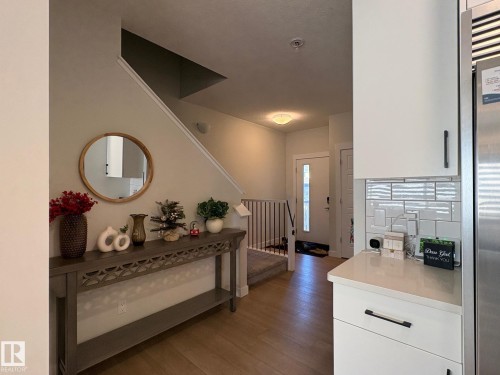 Entryway featuring wood-finish flooring extending to the staircase, a white front door with frosted glass detailing, and a white staircase railing - 9952 227 Street, Edmonton, AB 