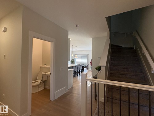 Hallway featuring wood-finish flooring, a powder room, and a carpeted staircase with a white railing and black spindles - 9952 227 Street, Edmonton, AB 
