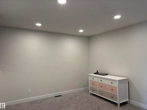 Recessed ceiling lighting illuminating a neutral-toned room with carpet flooring and white baseboards - 9952 227 Street, Edmonton, AB 