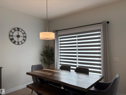 Dining area featuring a contemporary drum pendant light, wood-finish flooring, and a large window with horizontal blinds and drapery - 9952 227 Street, Edmonton, AB 