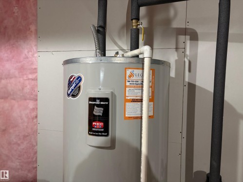 Bradford White water heater unit with insulated piping and a brass shut-off valve, positioned against drywall and visible pink insulation - 9952 227 Street, Edmonton, AB 