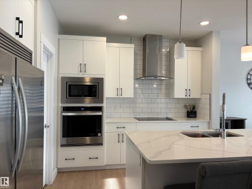 Modern kitchen featuring white cabinetry, stainless steel appliances, a subway tile backsplash, and a large island with an undermount sink - 9952 227 Street, Edmonton, AB 