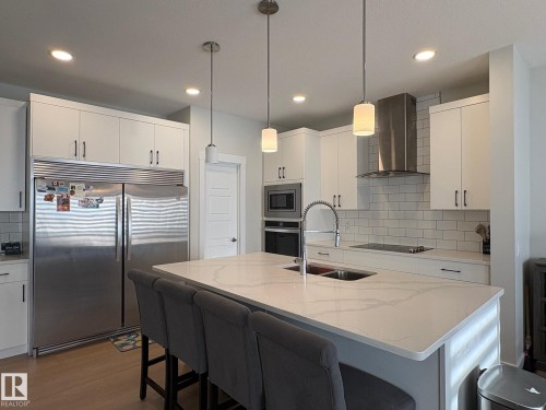 Modern kitchen featuring white cabinetry, a large center island with a double sink, stainless steel appliances, and a subway tile backsplash - 9952 227 Street, Edmonton, AB 